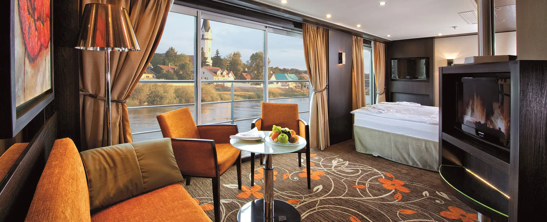Luxurious river cruise cabin with orange chairs, fireplace, and village view