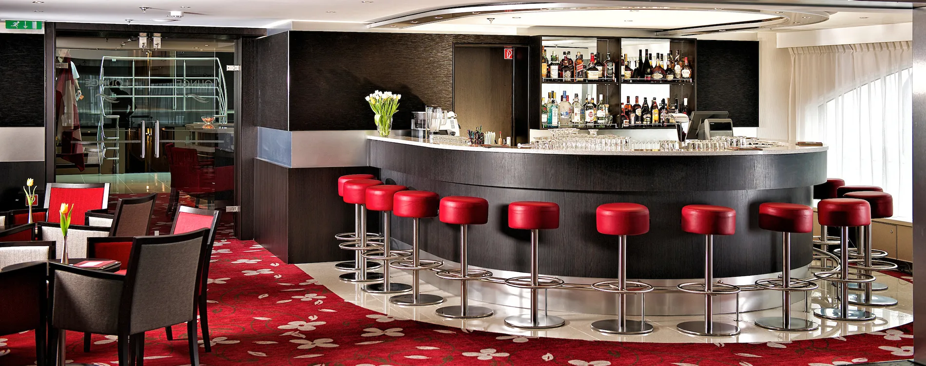 Modern bar with red stools, black counter, and floral carpet
