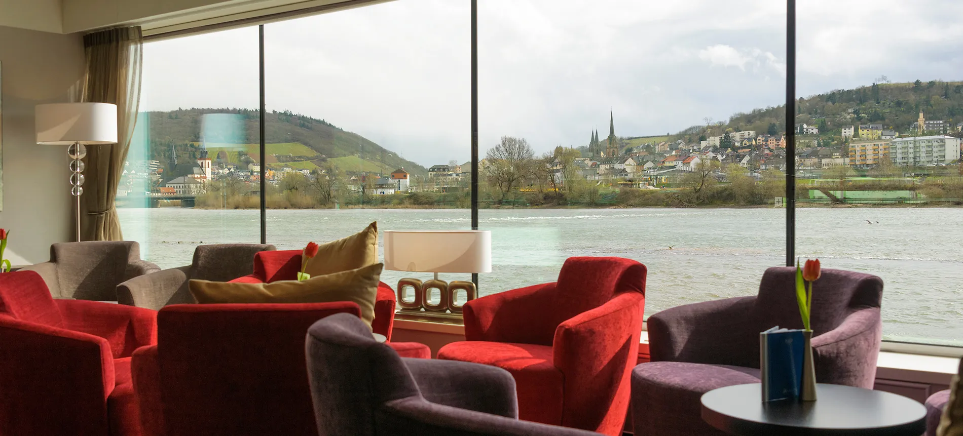 Cozy lounge with red chairs overlooking riverside town and scenic landscape