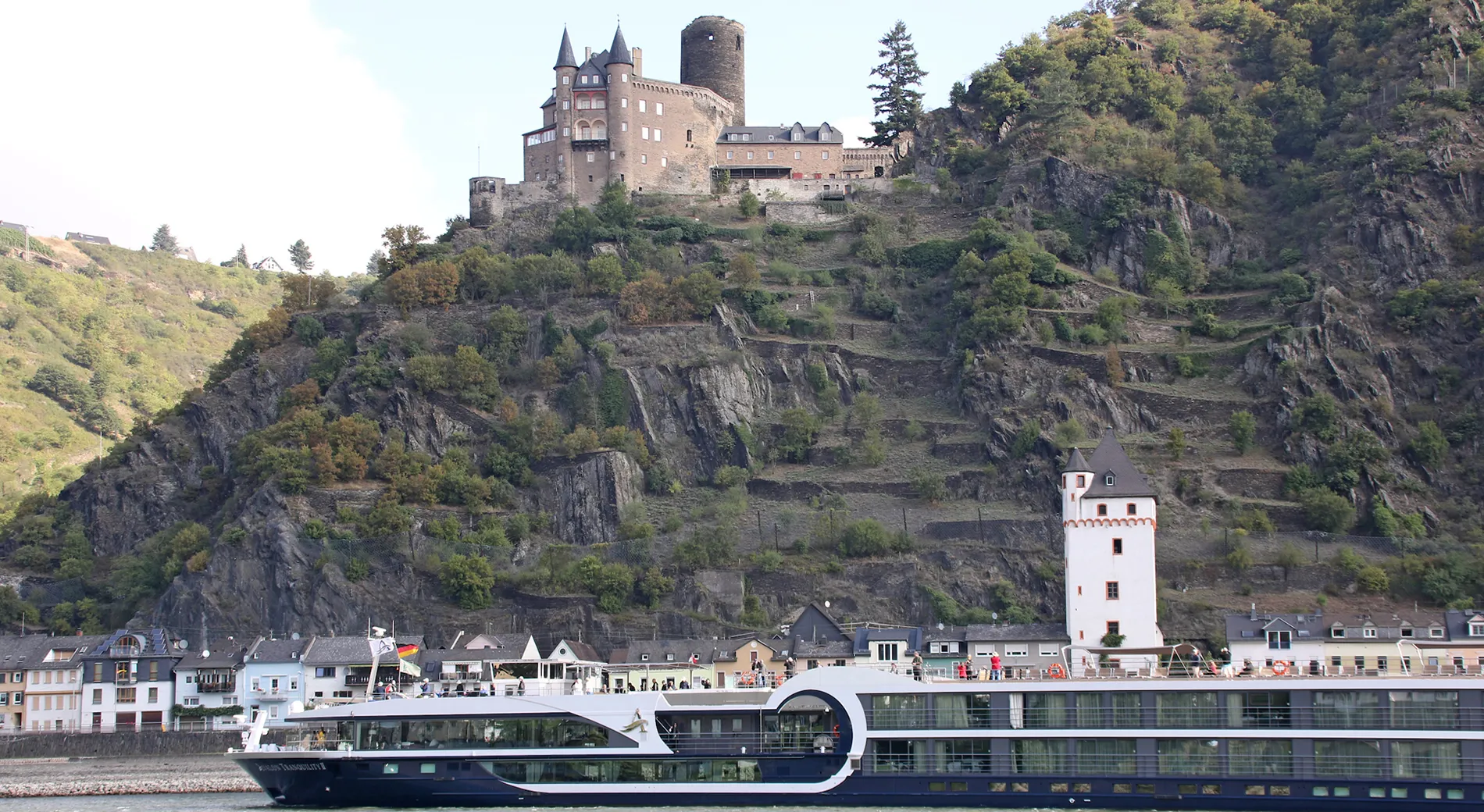 Medieval castle on rocky cliff overlooking river with modern cruise ship