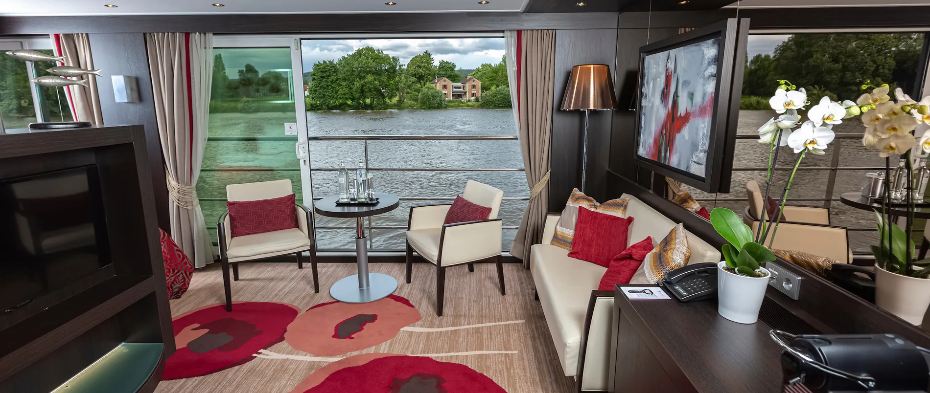 Luxury river cruise cabin with large windows, seating area, and scenic view