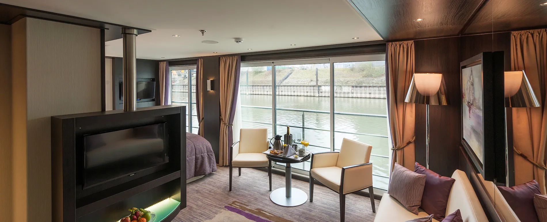 Luxury river cruise cabin with large windows, seating area, and water view