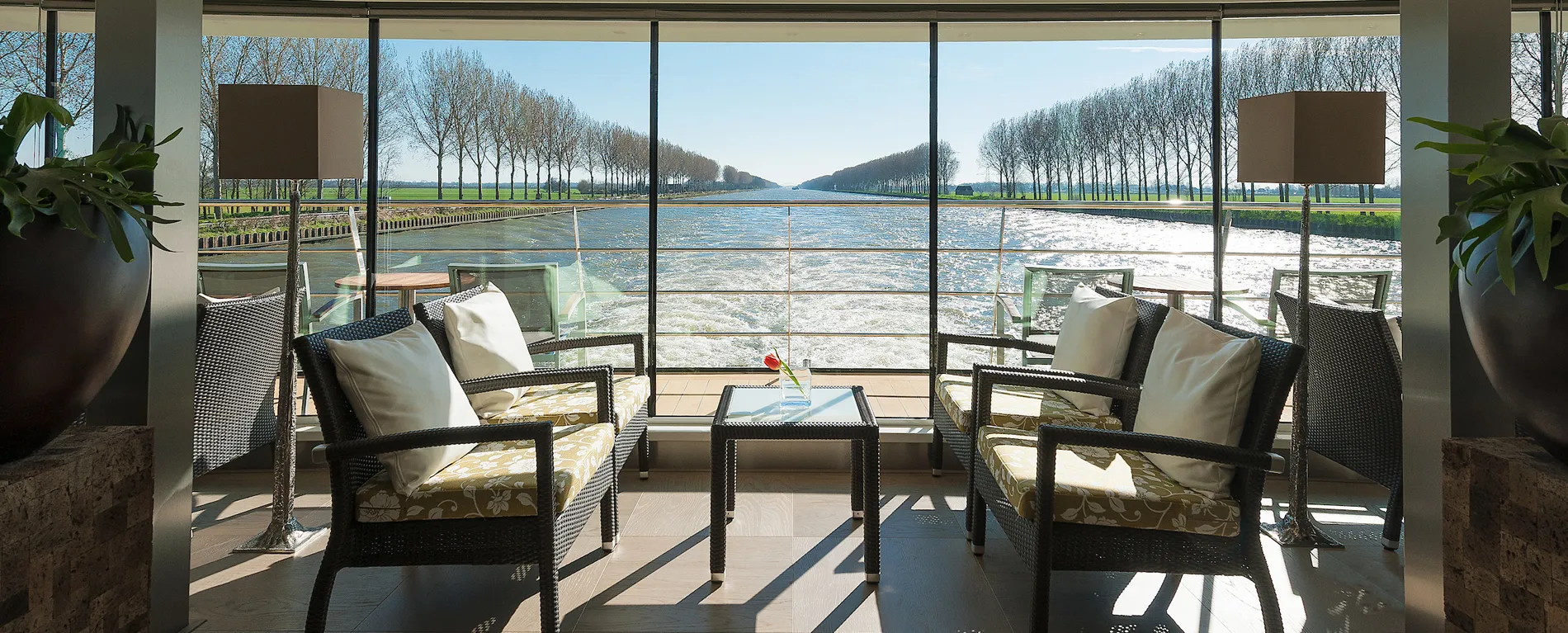 Indoor seating area with panoramic water view and tree-lined canal