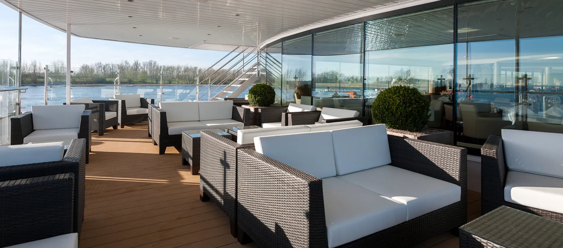 Modern glass-enclosed lounge with wicker furniture overlooking scenic river view