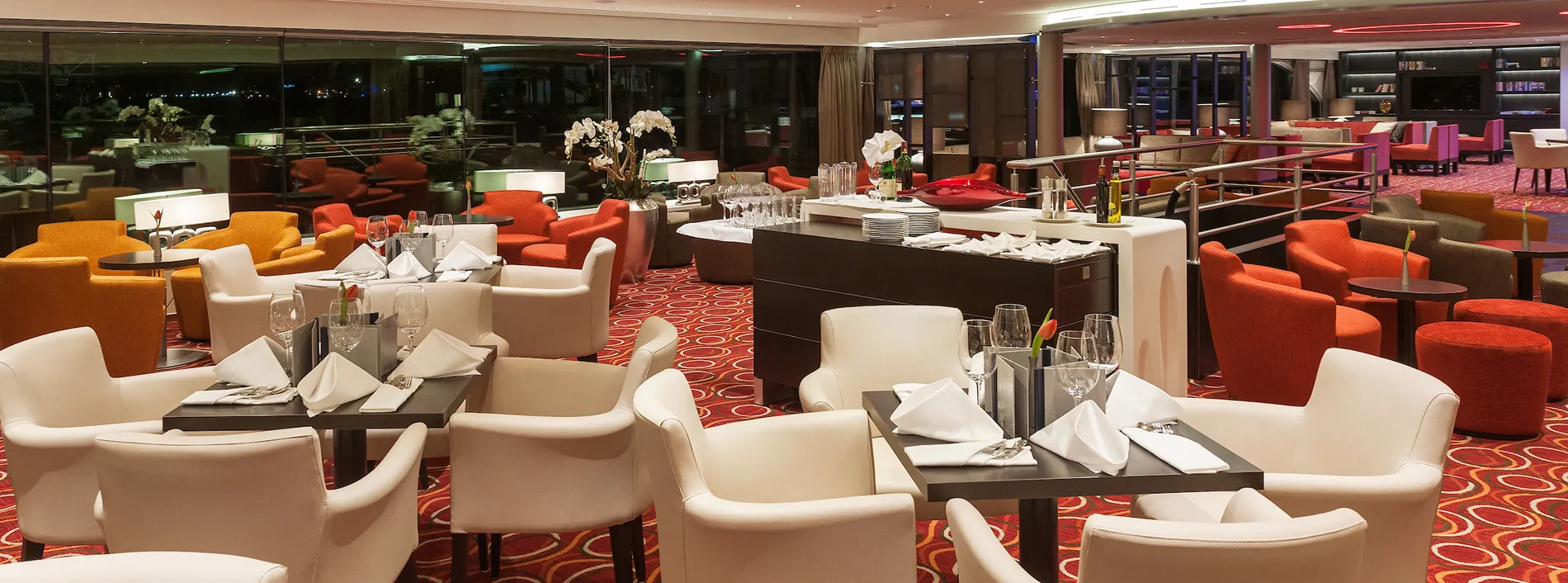 Modern restaurant lounge with white chairs, red carpet, and glass tables