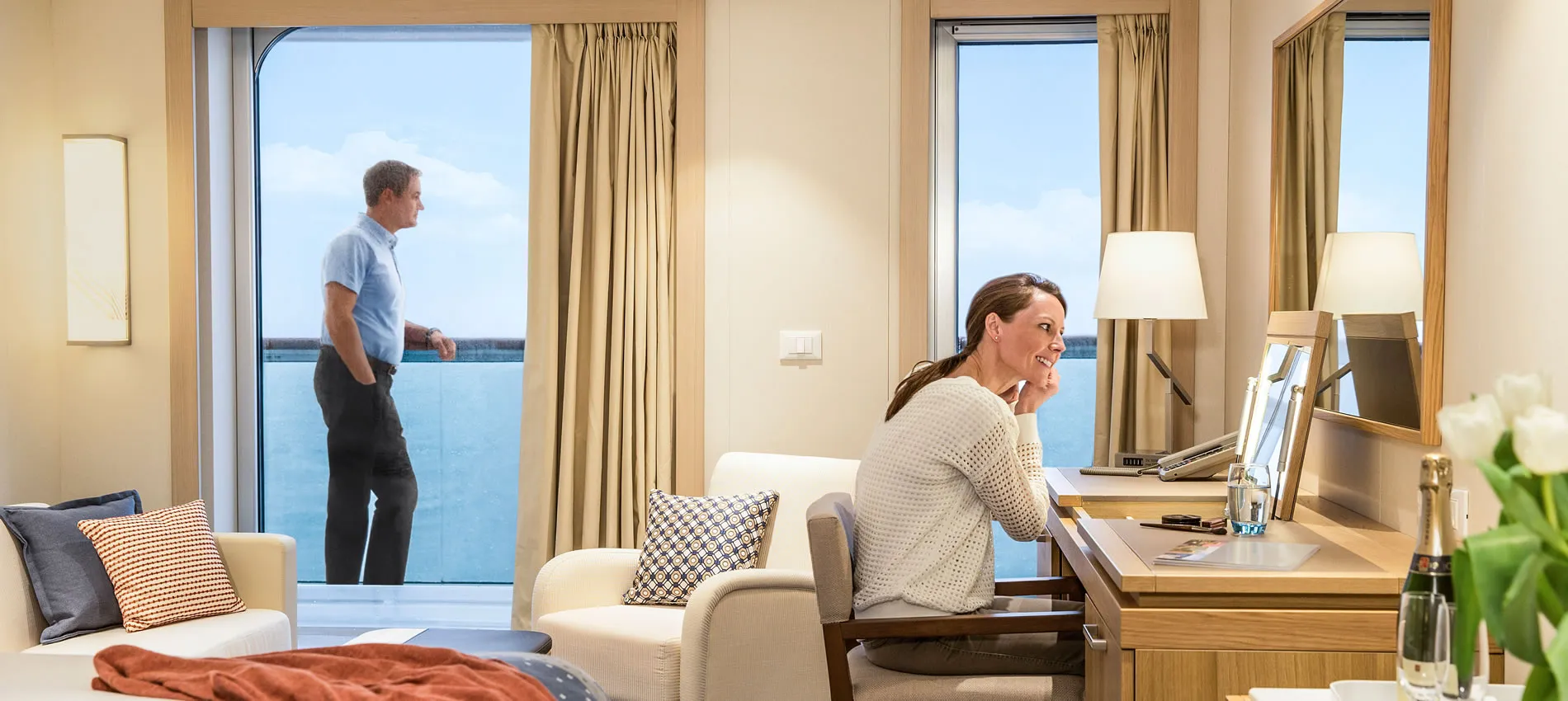 Cruise ship cabin with two people, ocean view, and comfortable seating