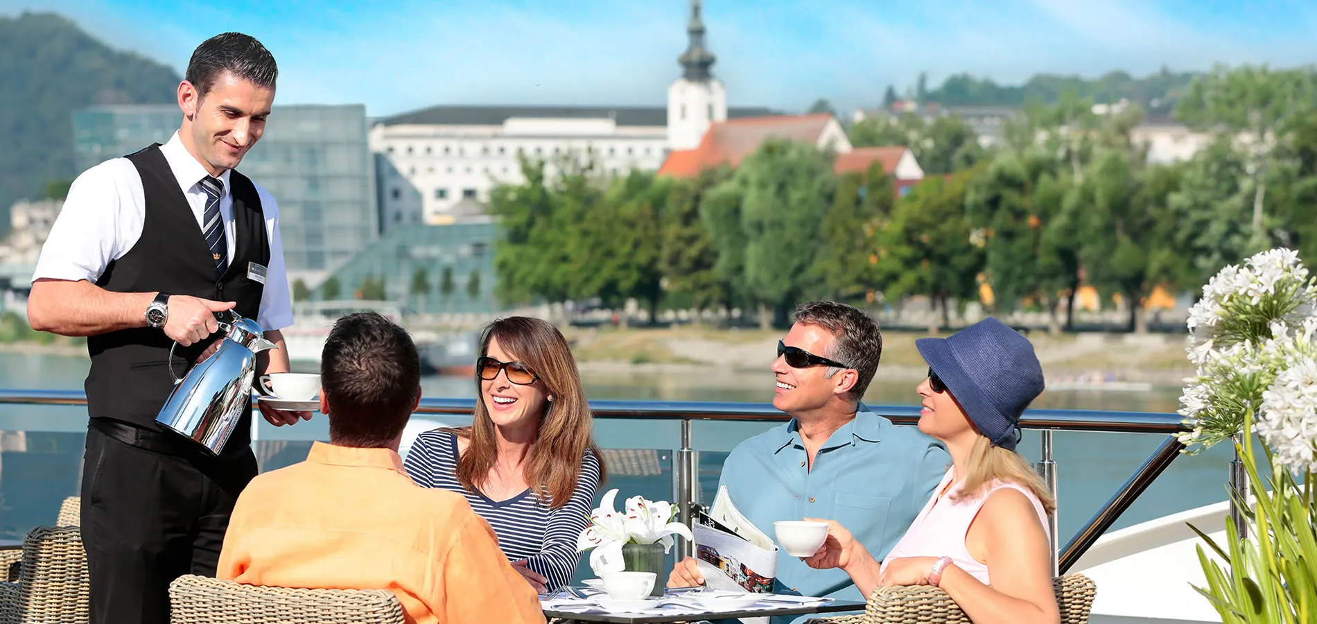 Waiter serving coffee to guests on outdoor terrace with city view
