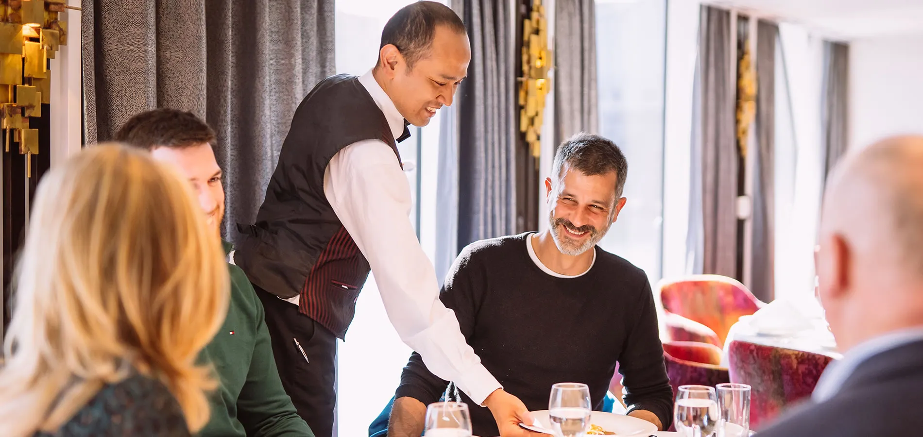 Waiter serving food to smiling guests at an elegant restaurant table