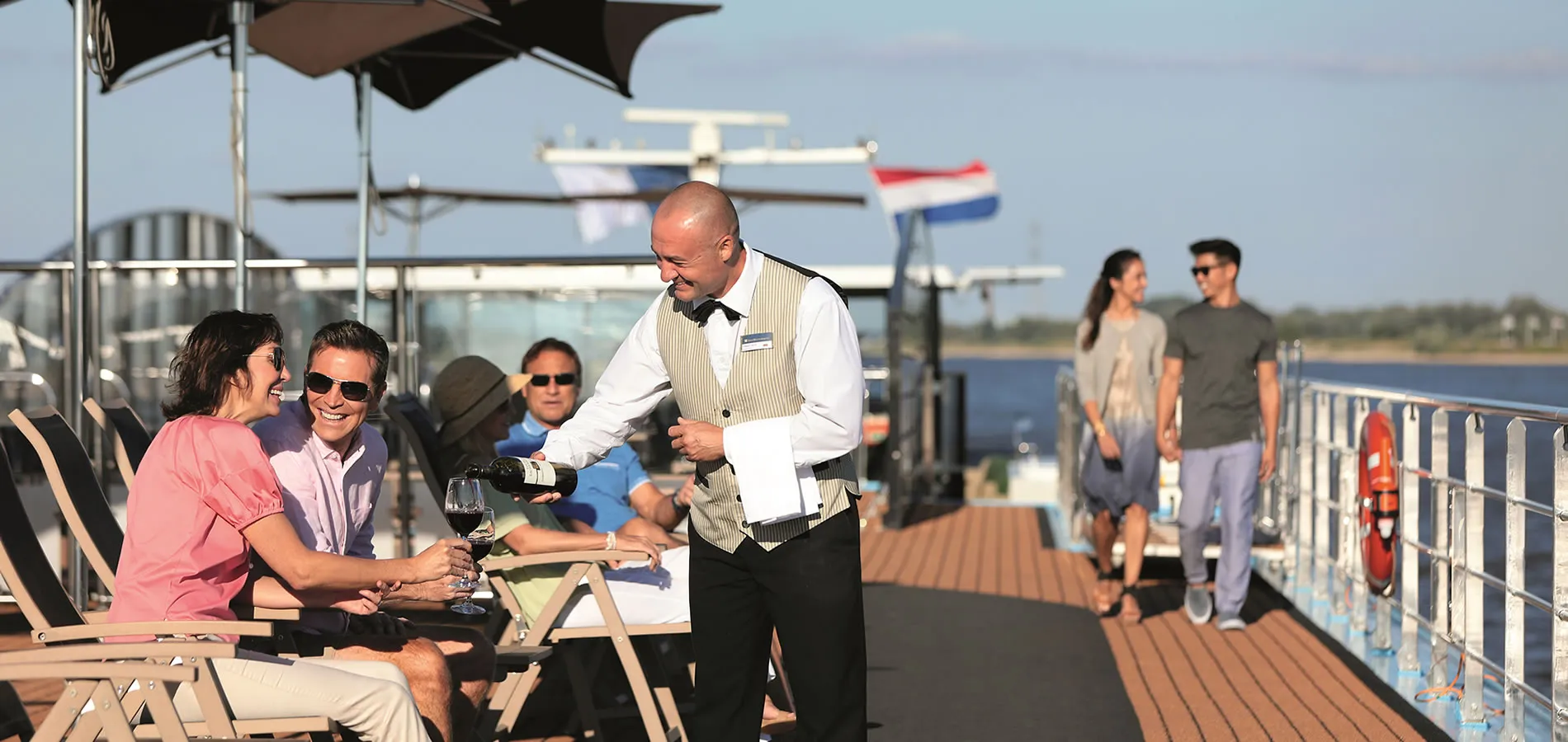 Waiter serving wine to guests on a sunny outdoor deck of a boat