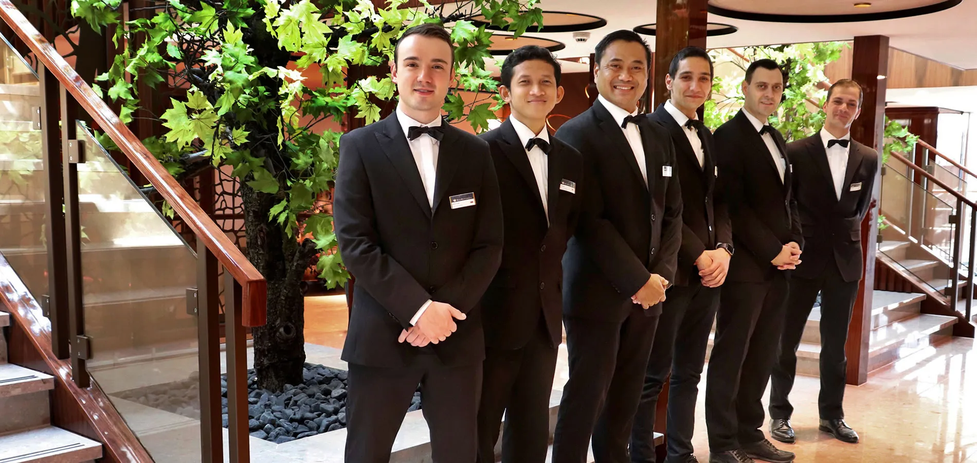 Hotel staff in tuxedos standing on stairs near decorative tree