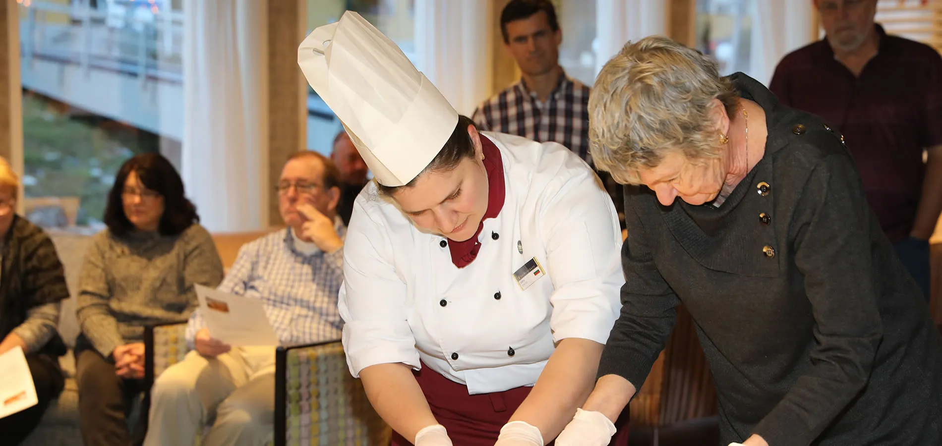 Chef in white uniform preparing food with assistance during culinary demonstration