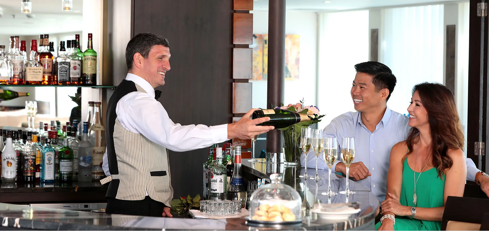 Bartender pouring champagne for smiling couple at elegant bar