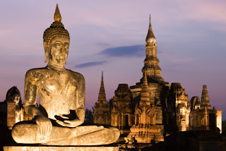 Golden Buddha statue at twilight with ancient temple ruins in background