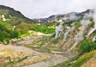Steaming geothermal valley with rocky terrain and green mountain slopes