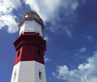 Red and white lighthouse against blue sky with fluffy clouds