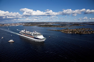 Large cruise ship sailing near coastline with blue sky and white clouds