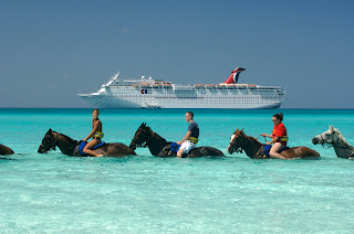 Riders on horseback in turquoise water with cruise ship in background