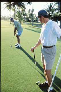 Two golfers on putting green, preparing to play their shots