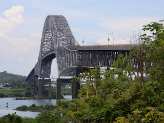 Large steel arch bridge crossing river surrounded by green trees and landscape