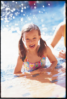 Smiling child splashing in water with colorful swimsuit on sunny day