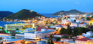 Coastal town at dusk with colorful buildings and hills overlooking harbor
