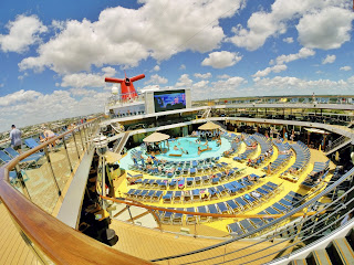 Cruise ship deck with colorful loungers, pool, and blue sky with clouds