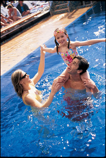 Family playing and splashing together in a bright blue swimming pool