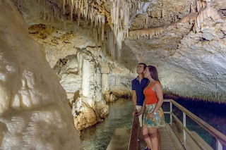 Tourists exploring rocky cave with stalactites on wooden walkway