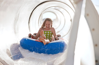 Child sitting in blue tube inside white curved tunnel slide