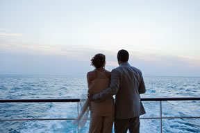Couple standing together on ship deck, overlooking calm ocean at dusk