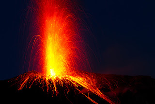 Volcanic eruption with bright orange lava shooting into dark night sky