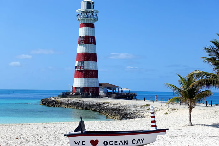 Red and white lighthouse on Ocean Cay beach with palm tree and boat