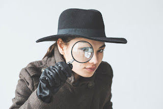 Detective wearing black hat and gloves looks through magnifying glass