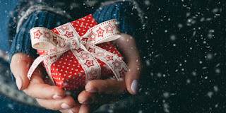 Hands holding wrapped Christmas gift with snowflakes falling in background