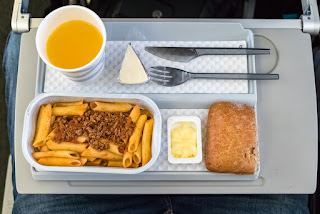 Airplane meal with pasta, bread, butter, and orange juice on tray