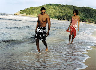 Two people walking along tropical beach with green hillside in background