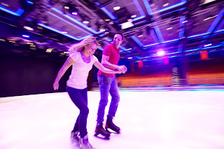 Two people skating together on a vibrant, colorful ice rink at night
