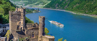 Medieval castle overlooking scenic Rhine River with cruise boat passing by