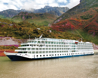 Large cruise ship sailing on river through scenic mountainous autumn landscape