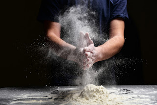 Baker clapping hands with flour, creating a dramatic cloud of white dust