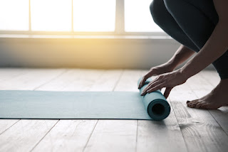 Person unrolling yoga mat on wooden floor near bright window