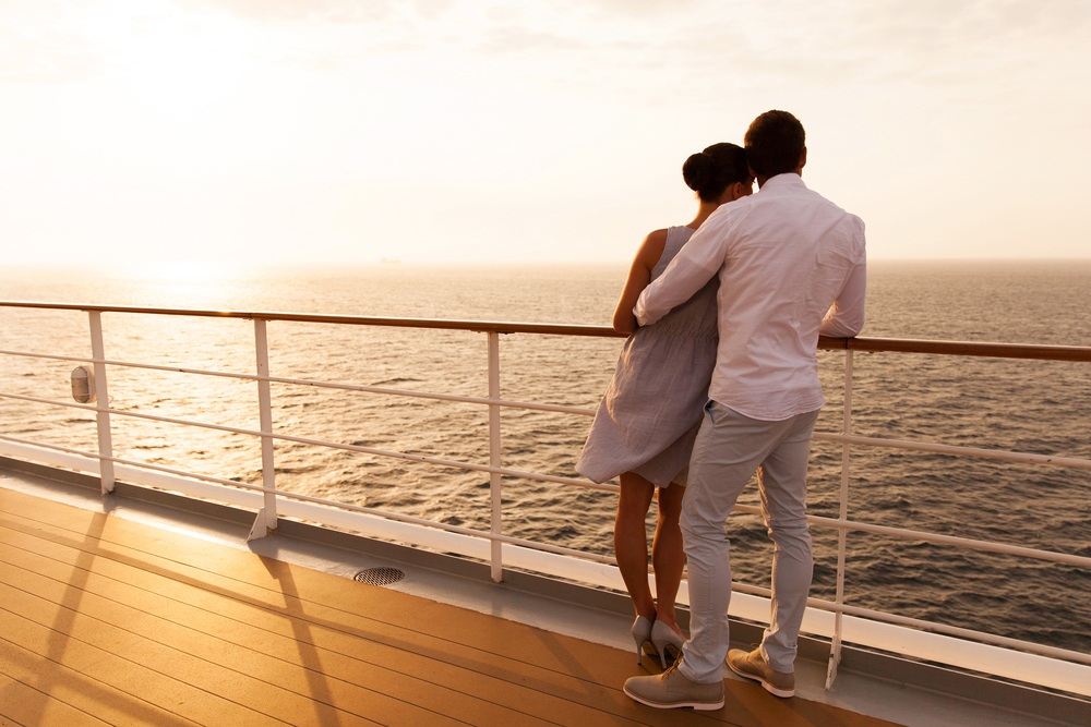 Couple embracing on cruise ship deck at sunset, overlooking ocean horizon