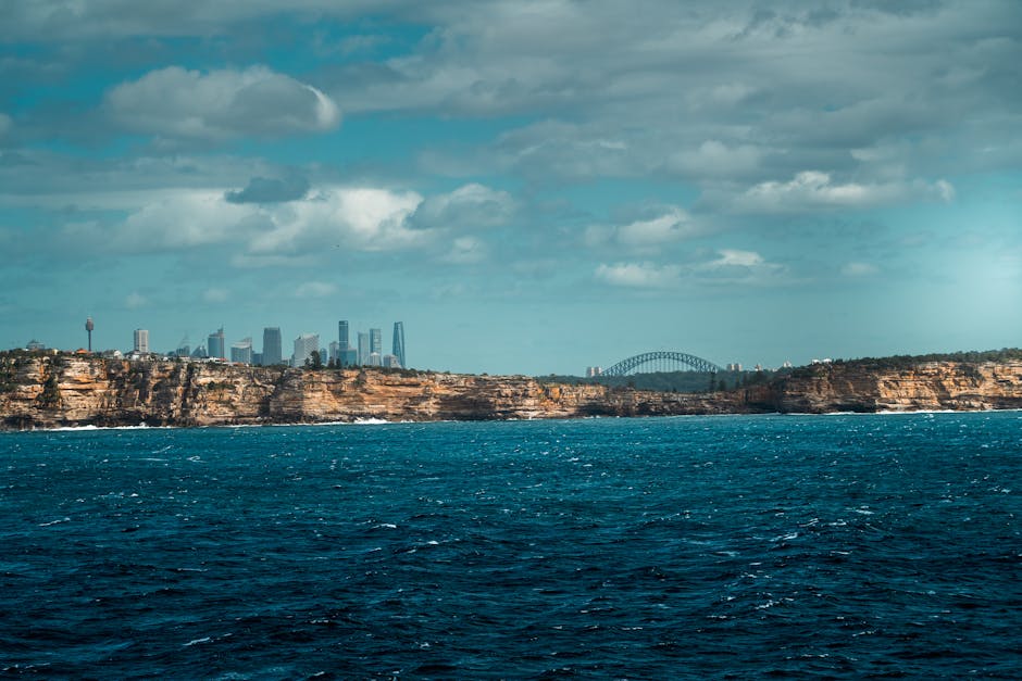 Dramatic coastal cliffs with the Sydney skyline and Harbour Bridge in the background.