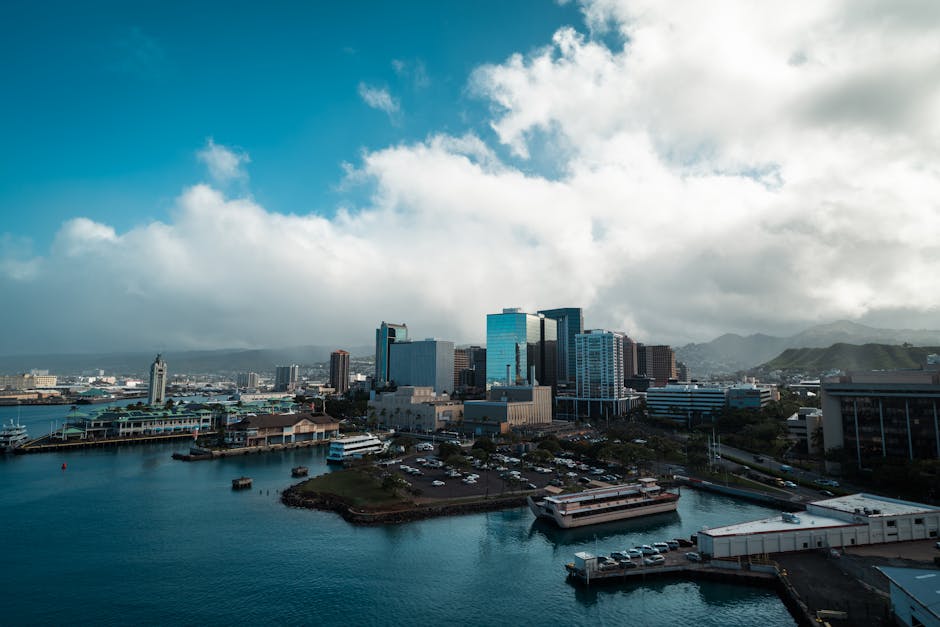 Honolulu harbour panorama featuring the city skyline with high-rise buildings set against a backdrop of lush green mountains, capturing the iconic port arrival scene for cruise travellers.