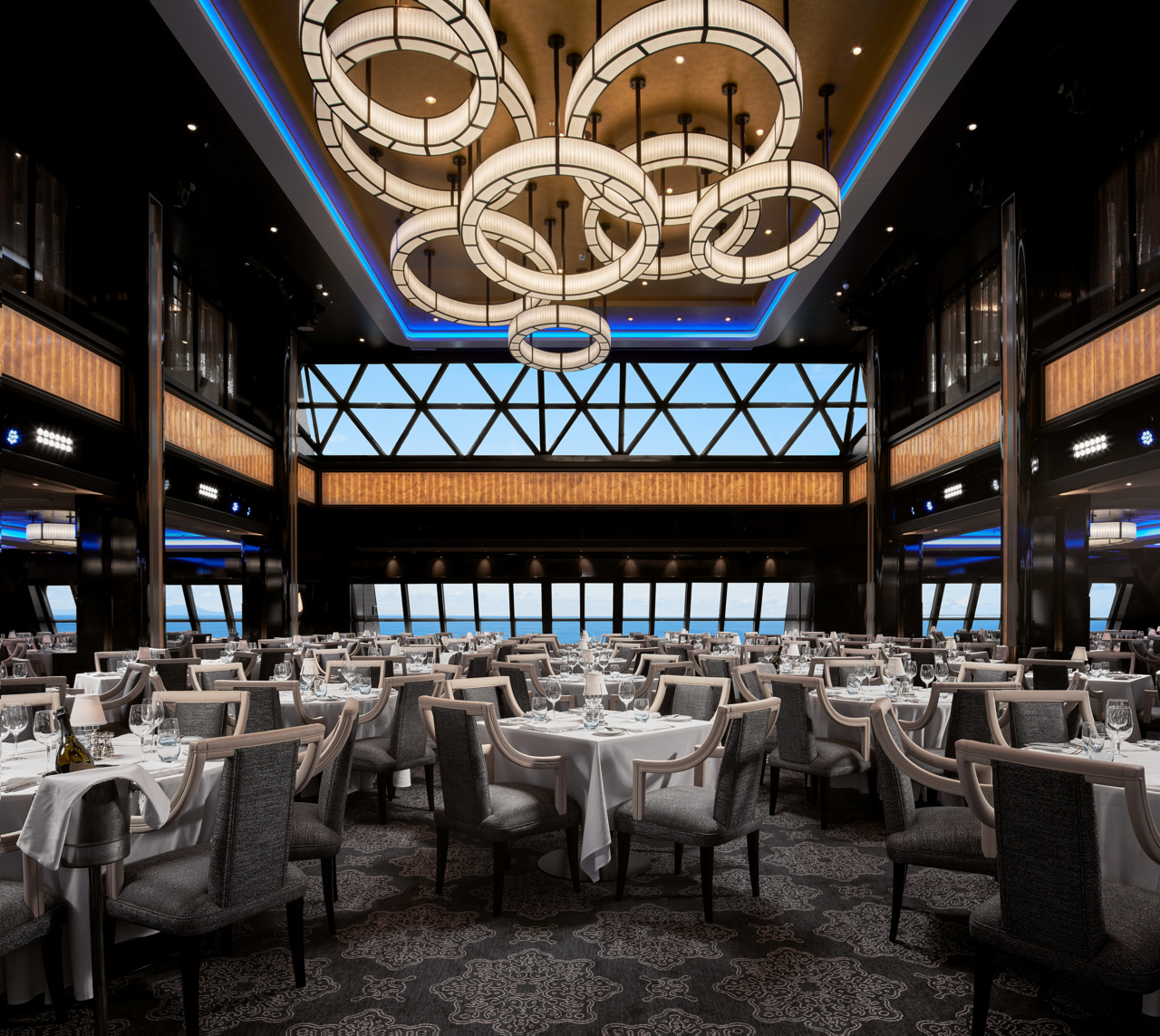 Elegant Manhattan Room dining space aboard Norwegian Encore with warm lighting and refined table settings.