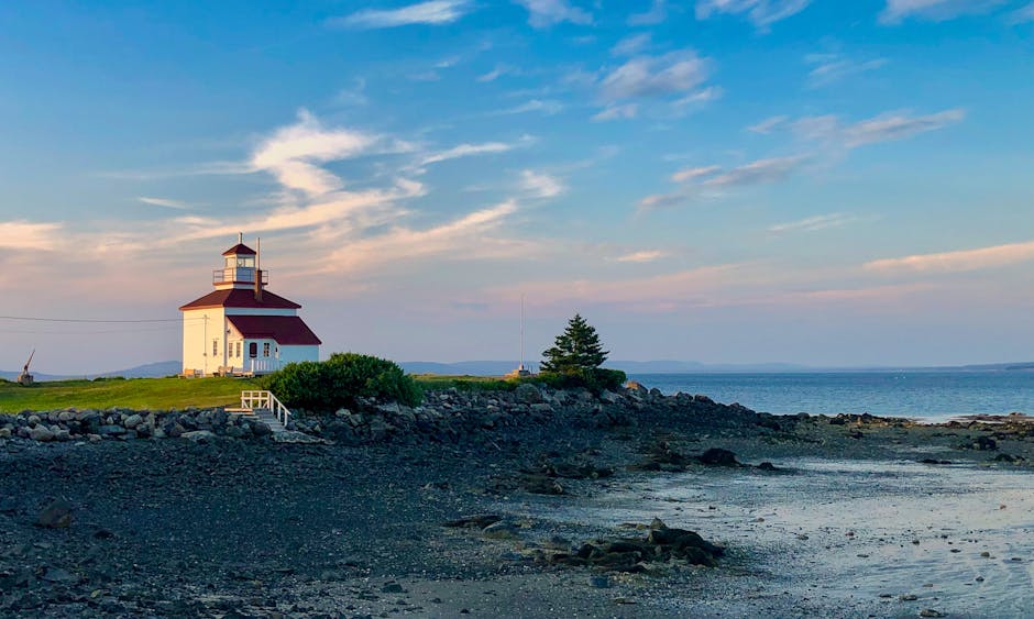 Picturesque Gilberts Cove lighthouse with rocky shore in Nova Scotia at sunset.