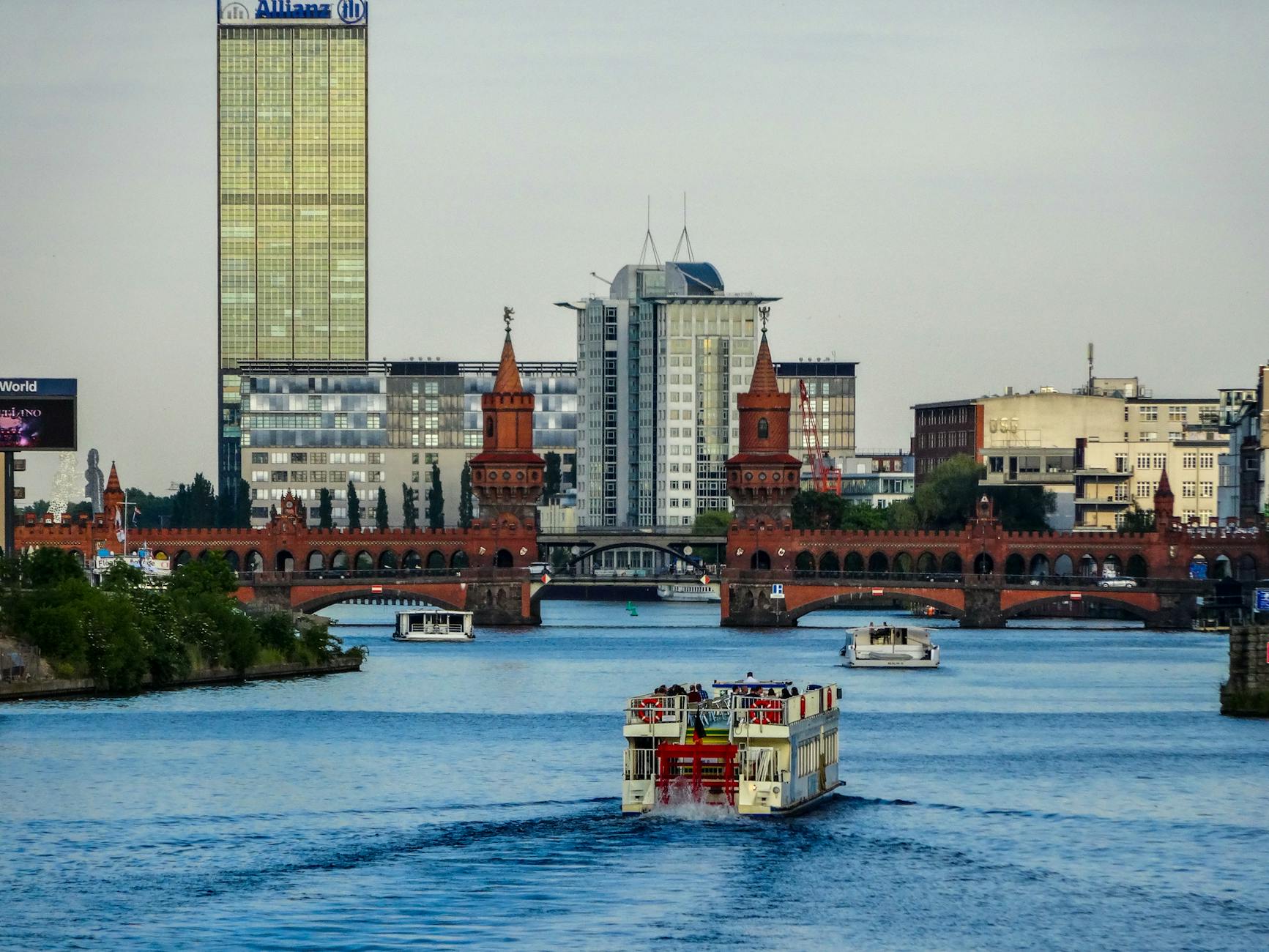 A scenic view of the Oberbaum Bridge over the Spree River in Berlin with a ferry passing beneath.
