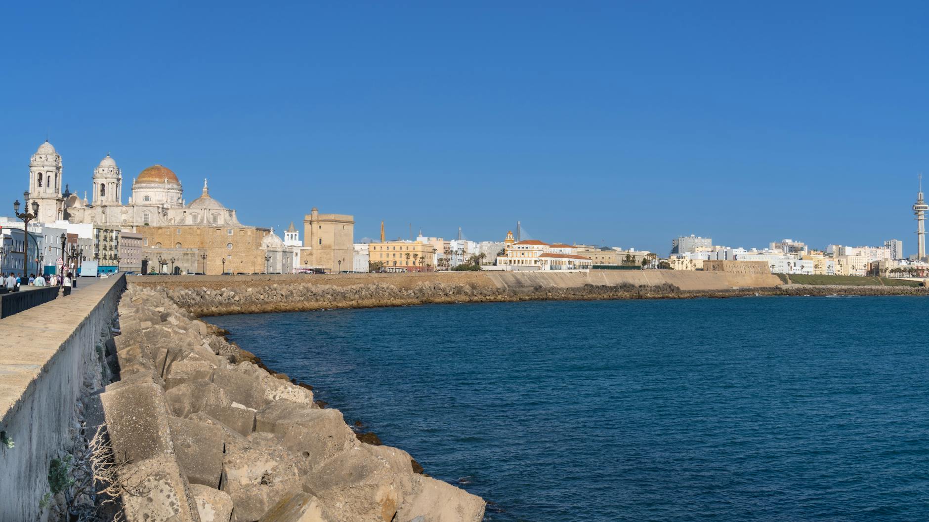 Panoramic view of the Cádiz waterfront showing the golden-domed cathedral rising above whitewashed buildings along the Atlantic seafront under clear blue skies