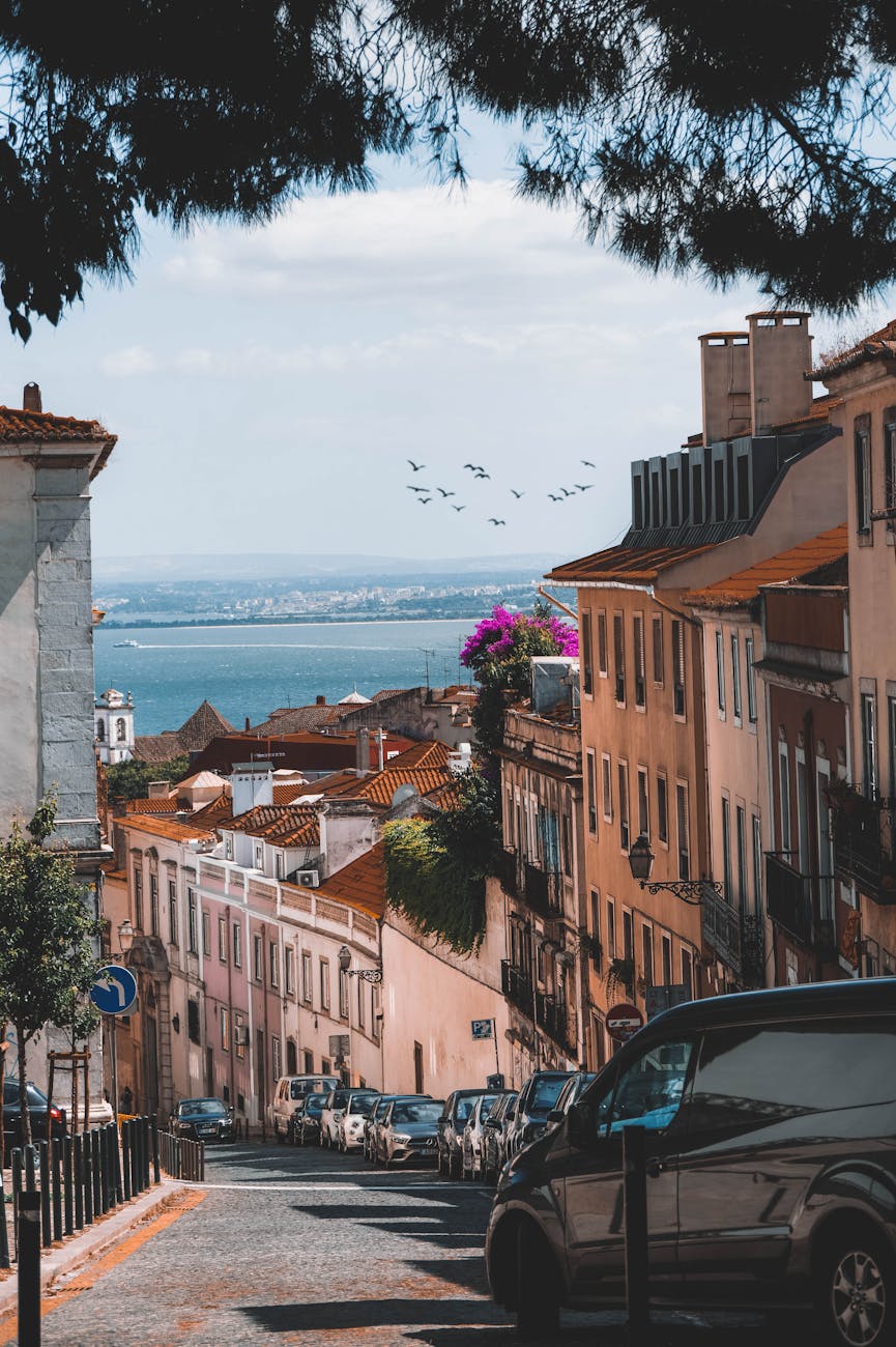 Scenic Lisbon street with ocean view, colorful buildings, and cars on a sunny day.