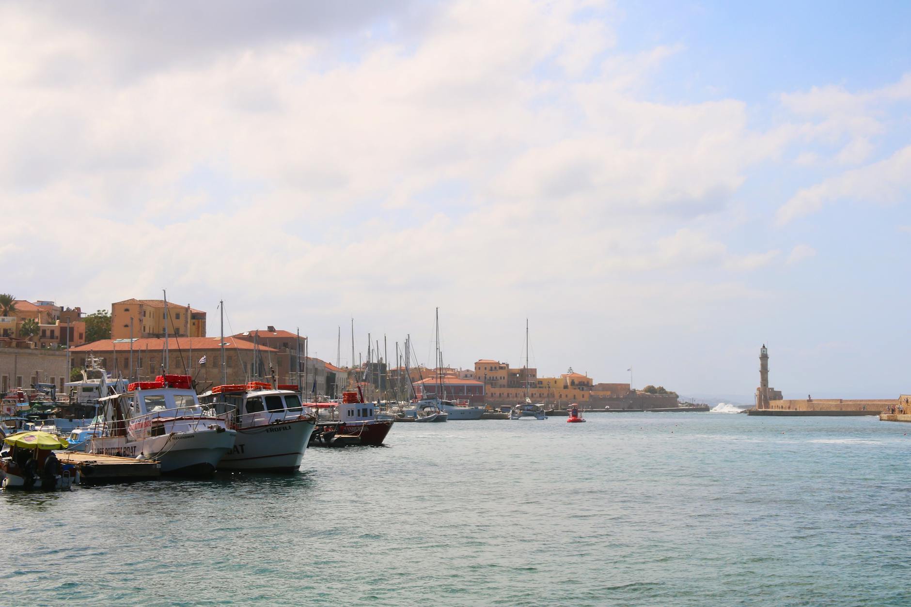 Chania's Venetian harbor featuring historic stone architecture and traditional boats moored along the waterfront under warm, bright Mediterranean sunlight
